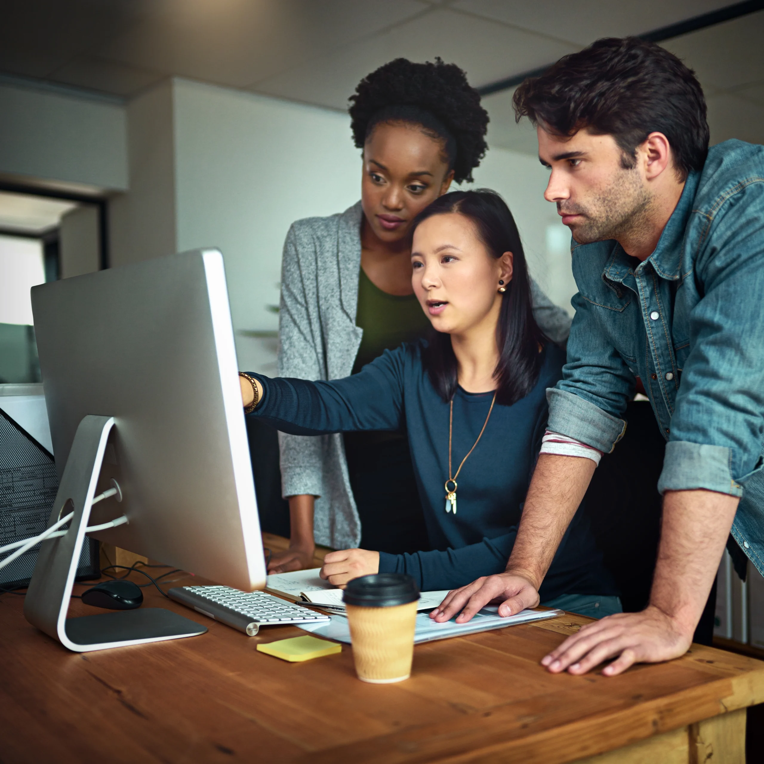 Three people work on a computer monitor, in discussion