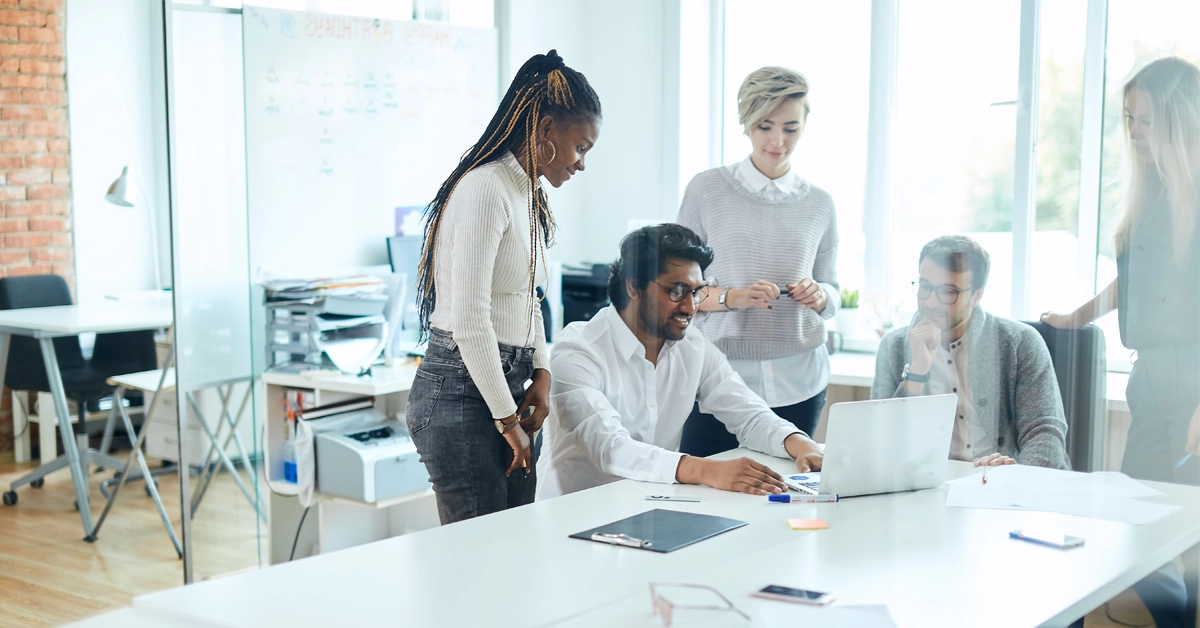 Five people in discussion around a laptop in a modern office