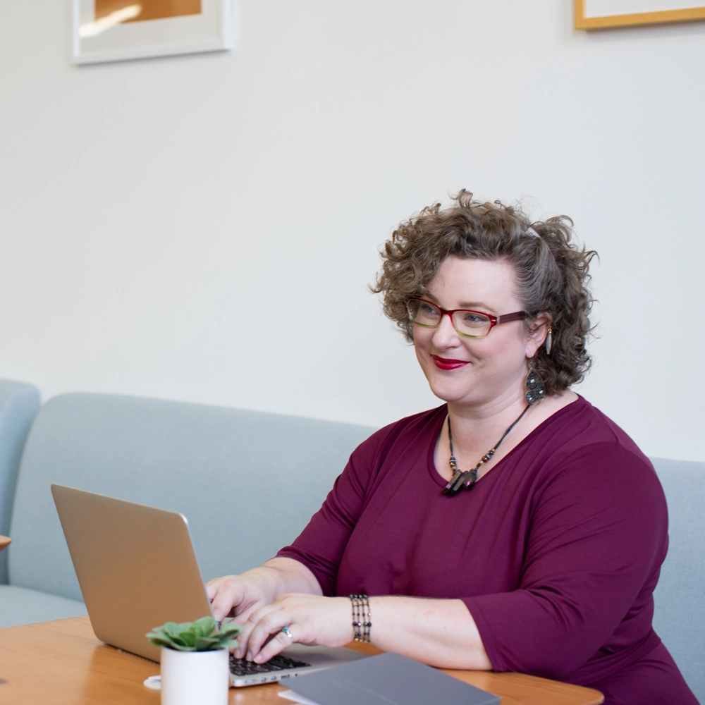 GLYNT_WP_7Questions_Pic3 A smiling woman works on a laptop