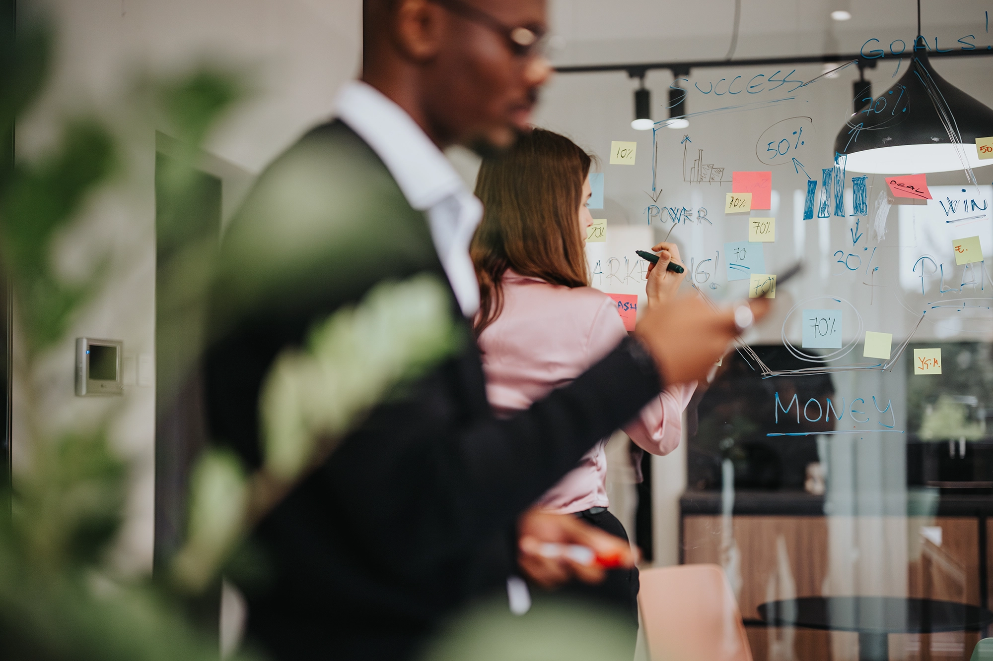 Two coworkers making notes on a transparent white board