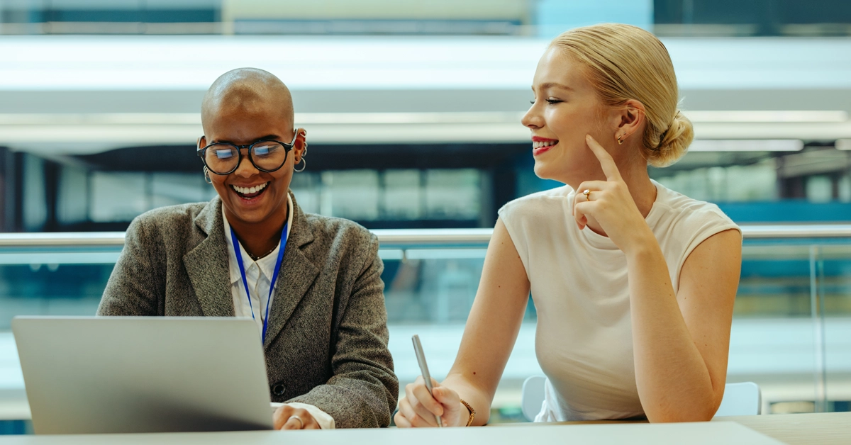 Two women in a modern office talk over a laptop