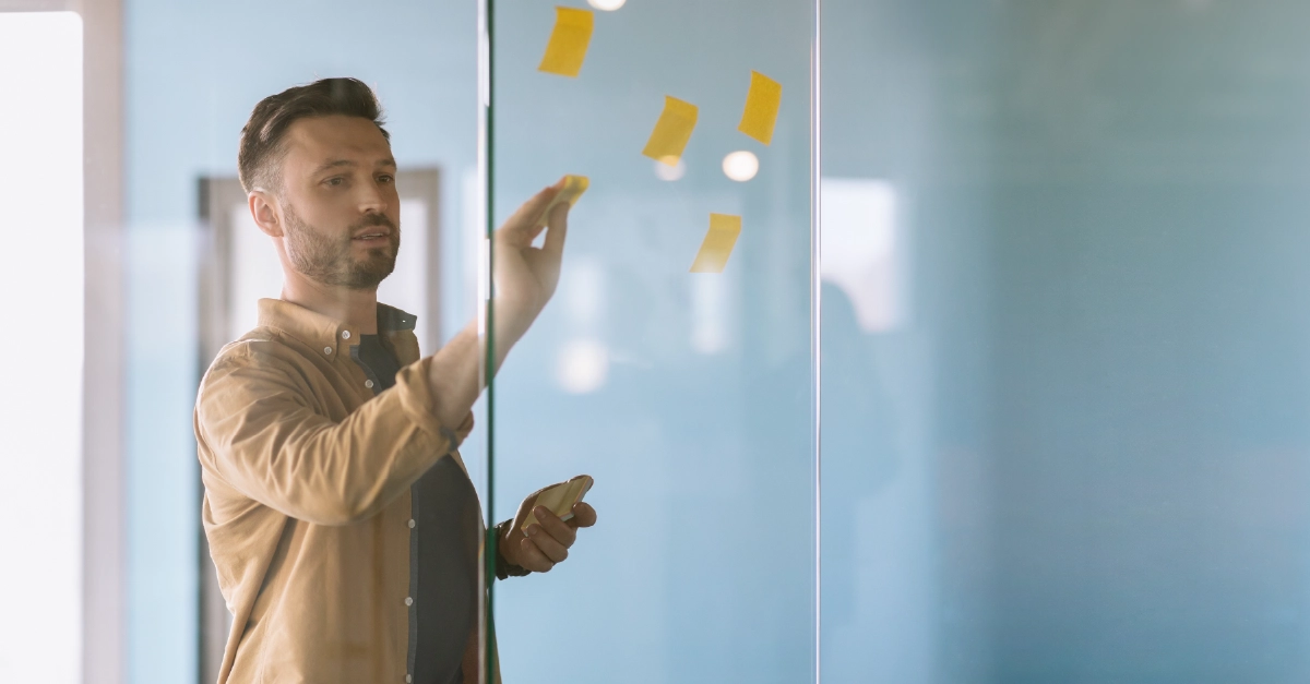 A man adds sticky notes to a transparent project board
